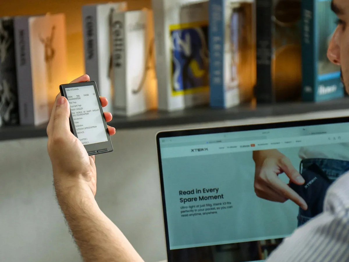 Xteink X3 dipegang di depan laptop, menampilkan daftar isi buku